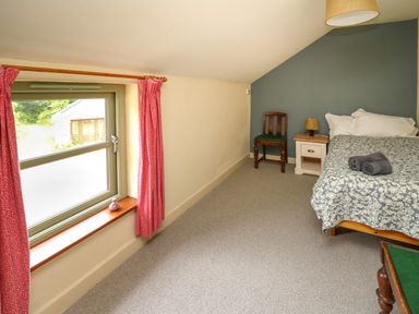 A bedroom with a bed a nightstand a chair a window with red curtains and a lamp at Taibach in Dinas Cross