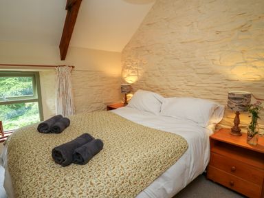 A bedroom with a double bed featuring white sheets and rolled towels on a patterned blanket at Taibach in Dinas Cross