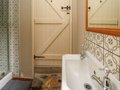 A bathroom with a white sink and chrome taps a wooden door and patterned tiles on the wall at Taibach in Dinas Cross