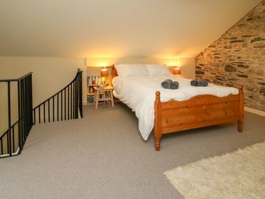 A bedroom with a wooden bed with white bedding two bedside lamps a stone wall and a staircase with a black railing at Taibach in Dinas Cross