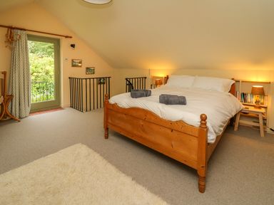A bedroom with a wooden bed with white bedding two rolled towels bedside tables with lamps books a green glass door and a carpet at Taibach in Dinas Cross