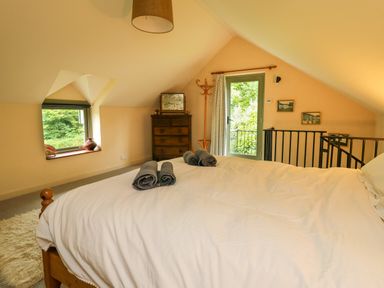 A bedroom with a wooden bed with white bedding and gray towels on it wooden chest of drawers a window and a door leading outside at Taibach in Dinas Cross