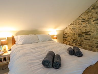 A bedroom with a bed with white bedding rolled towels on the bed stone wall and bedside tables with lamps at Taibach in Dinas Cross