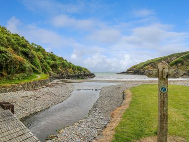 A rocky beach with a small creek flowing into the sea and a wooden signpost on the grass at Taibach in Dinas Cross