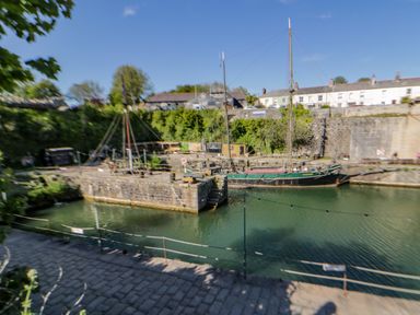 A dock with sailboats moored in the water near stone buildings and cobblestone path at Quay House in Charlestown