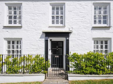 A white stone house front with black door and metal gate with green shrubs at Quay House in Charlestown