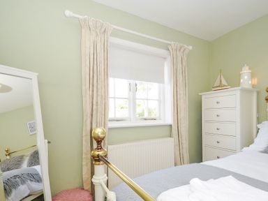 A bedroom with a window white curtains a white chest of drawers and a bed with folded towels at Quay House in Charlestown