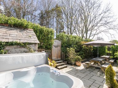 An outdoor patio area with a hot tub wooden picnic tables with umbrellas and greenery at Quay House in Charlestown