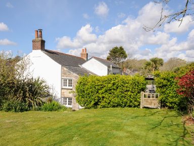 A garden with green lawn and shrubs next to a white and stone house with chimneys at Quay House in Charlestown
