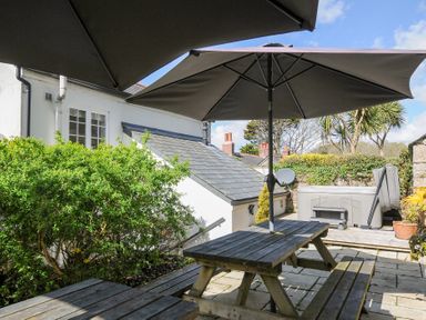 An outdoor patio with wooden picnic tables and umbrellas next to a white house and greenery at Quay House in Charlestown