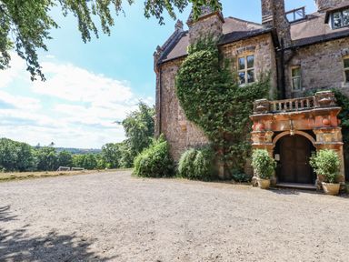 An old stone building with a gravel driveway green plants and trees in the background at Nethercott House in Iddesleigh near Hatherleigh