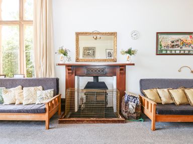 A living room with two wooden framed sofas with cushions a fireplace with a protective screen a mirror and flower vases at Nethercott House in Iddesleigh near Hatherleigh