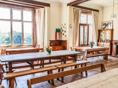 A dining room with wooden tables and benches and large windows at Nethercott House in Iddesleigh near Hatherleigh