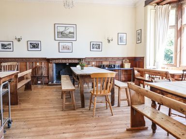 A dining room with wooden tables benches chairs black and white photos on the walls at Nethercott House in Iddesleigh near Hatherleigh