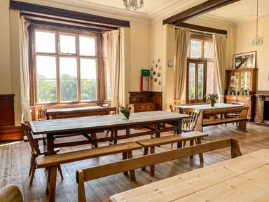 A dining room with wooden tables and benches and large windows at Nethercott House Iddesleigh near Hatherleigh