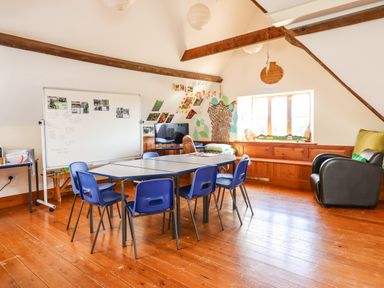 A classroom with blue chairs around tables a whiteboard on wheels and a leather armchair at Nethercott House in Iddesleigh near Hatherleigh