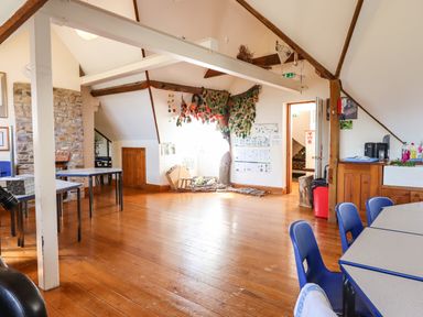A room with wooden floor tables and blue chairs a stone fireplace and a wall decorated with a fabric tree at Nethercott House in Iddesleigh near Hatherleigh