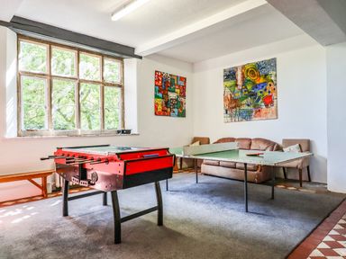 A game room with a foosball table a ping pong table chairs and abstract paintings on walls at Nethercott House in Iddesleigh near Hatherleigh