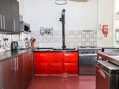 A kitchen with a red stove a microwave a kettle knives hanging on the wall and stainless steel cabinets at Nethercott House in Iddesleigh near Hatherleigh