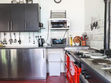 A kitchen with stainless steel cabinets utensils hanging on a rail a toaster oven microwave kettle red oven and kitchen knives on a tiled wall at Nethercott House in Iddesleigh near Hatherleigh