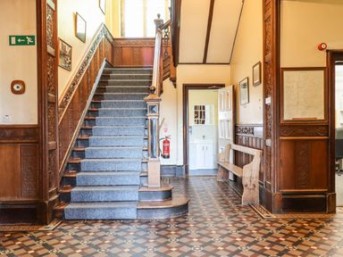A staircase with carpet runner and wooden paneling next to a wooden bench and open door showing bathroom at Nethercott House in Iddesleigh near Hatherleigh
