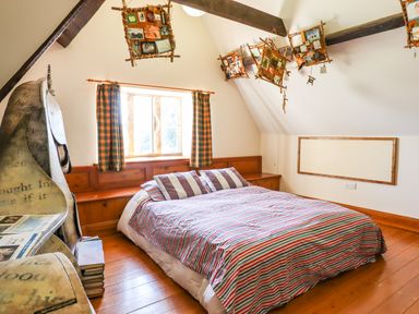 A bedroom with a bed and striped bedding wooden floor and window with checkered curtains at Nethercott House in Iddesleigh near Hatherleigh