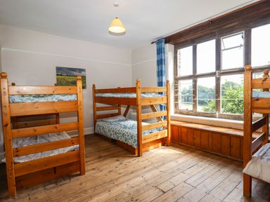 A bedroom with three wooden bunk beds a large window and wooden flooring at Nethercott House in Iddesleigh near Hatherleigh
