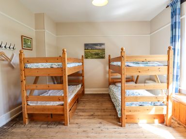 A bedroom with two wooden bunk beds and a window with blue curtains at Nethercott House in Iddesleigh near Hatherleigh