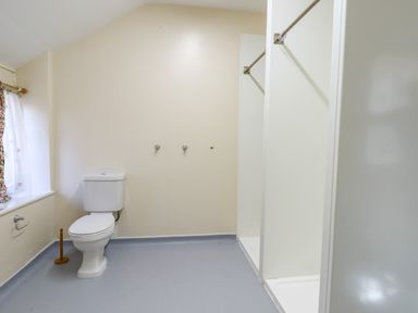 A bathroom with a toilet a shower area and a window with curtains at Nethercott House in Iddesleigh near Hatherleigh
