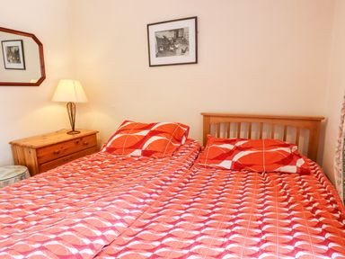 A bedroom with two beds covered with patterned red bedding a wooden nightstand with a lamp and a framed picture on the wall at Nethercott House in Iddesleigh near Hatherleigh