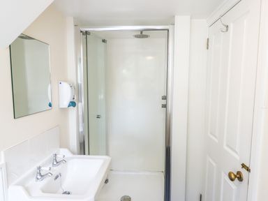 A bathroom with a white sink a wall mirror a soap dispenser a shower with glass doors and a white door at Nethercott House in Iddesleigh near Hatherleigh