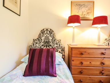 A bedroom with a patterned headboard a purple cushion on a bed a wooden chest of drawers and two lamps at Nethercott House in Iddesleigh near Hatherleigh