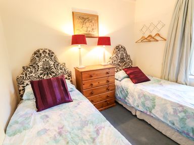 A bedroom with two single beds with patterned headboards a wooden chest of drawers with two red lamps and a picture above at Nethercott House in Iddesleigh near Hatherleigh