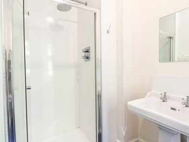 A bathroom with a glass shower enclosure and a white sink with two taps and a mirror at Nethercott House in Iddesleigh near Hatherleigh