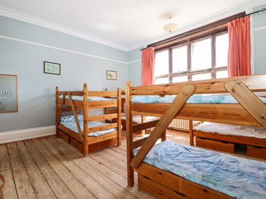 A bedroom with wooden bunk beds wooden floor and large window with curtains at Nethercott House in Iddesleigh near Hatherleigh