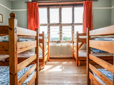 A bedroom with four wooden bunk beds and a large window with orange curtains at Nethercott House Iddesleigh near Hatherleigh