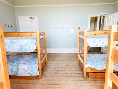 A room with two wooden bunk beds with patterned bedding a door and a coat rack on the wall at Nethercott House in Iddesleigh near Hatherleigh