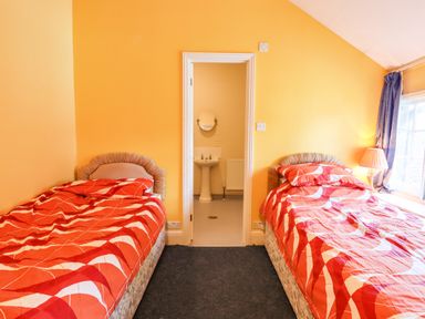 A bedroom with two single beds with red patterned bedding and an adjacent bathroom at Nethercott House in Iddesleigh near Hatherleigh