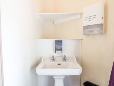 A white sink with two taps under white shelves and a wall-mounted soap dispenser at Nethercott House in Iddesleigh near Hatherleigh