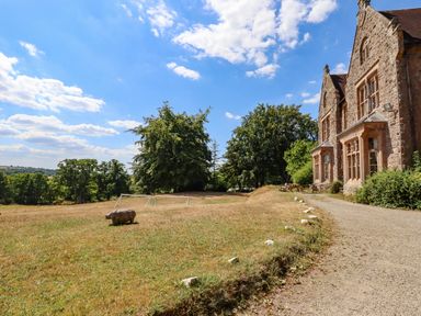 A stone house with multiple windows next to a gravel path and grassy field with soccer goals and trees at Nethercott House Iddesleigh near Hatherleigh
