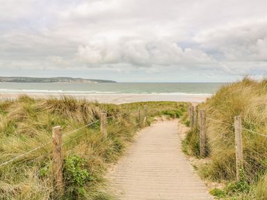 A pathway through grass dunes leading to a sandy beach and ocean at Rose in Illogan
