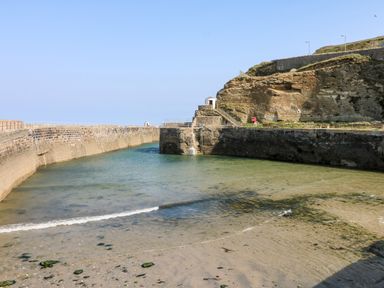 A coastal harbor with stone walls and clear shallow water at Rose in Illogan