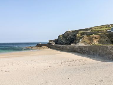 A sandy beach with a stone seawall and rocky cliffs by the sea at Rose in Illogan