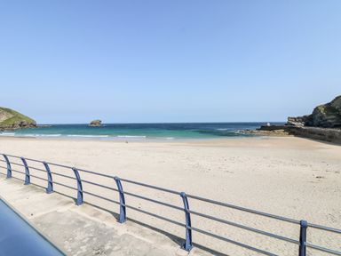 A sandy beach with a metal railing and a view of the ocean and rocky hills at Rose in Illogan