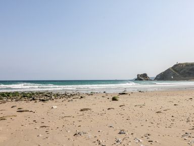 A sandy beach with scattered rocks and waves near a rocky cliff at Rose in Illogan