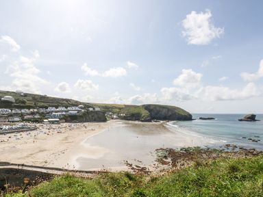A sandy beach with people, houses on a hillside, rocky cliffs, and the sea at Rose in Illogan
