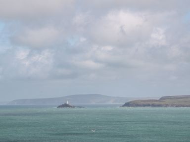A lighthouse on a small island in the sea with distant hills and cloudy sky at Rose in Illogan