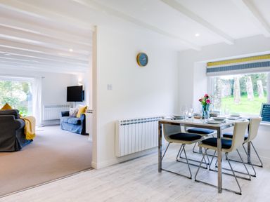 A dining area with table and four chairs beside a window and a living room with sofas and a wall-mounted TV at Goose Cottage within the Helland Barton Farm collection Delabole