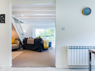 A living room with a dark sofa and a beige armchair near stairs and a sliding glass door at Goose Cottage within the Helland Barton Farm collection Delabole