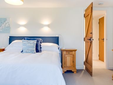 A bedroom with a double bed white bedding blue headboard wooden bedside cabinets and an open wooden door at Goose Cottage within the Helland Barton Farm collection Delabole